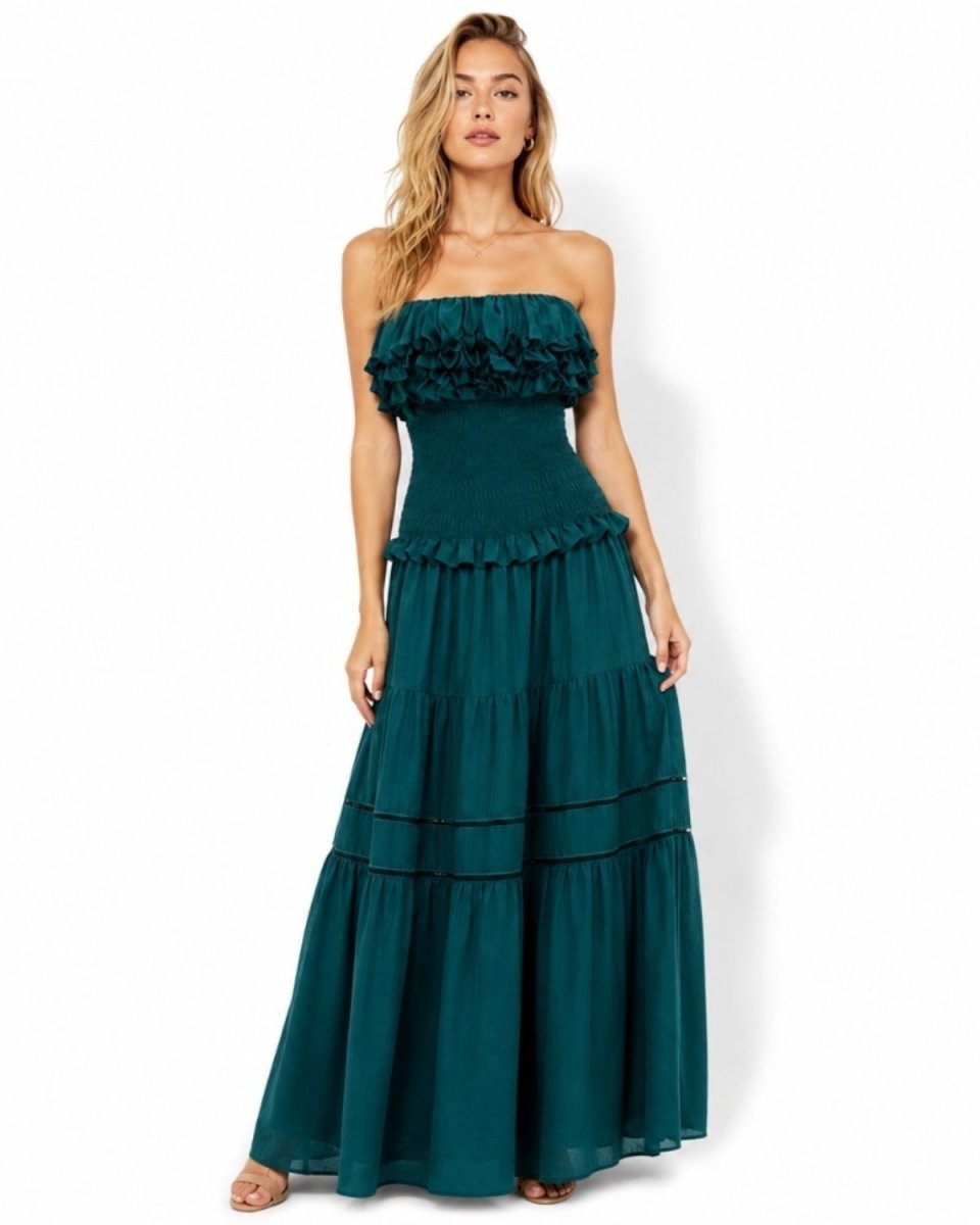 Woman wearing dark green strapless smocked tiered maxi dress with ruffle bodice looking directly at camera.
