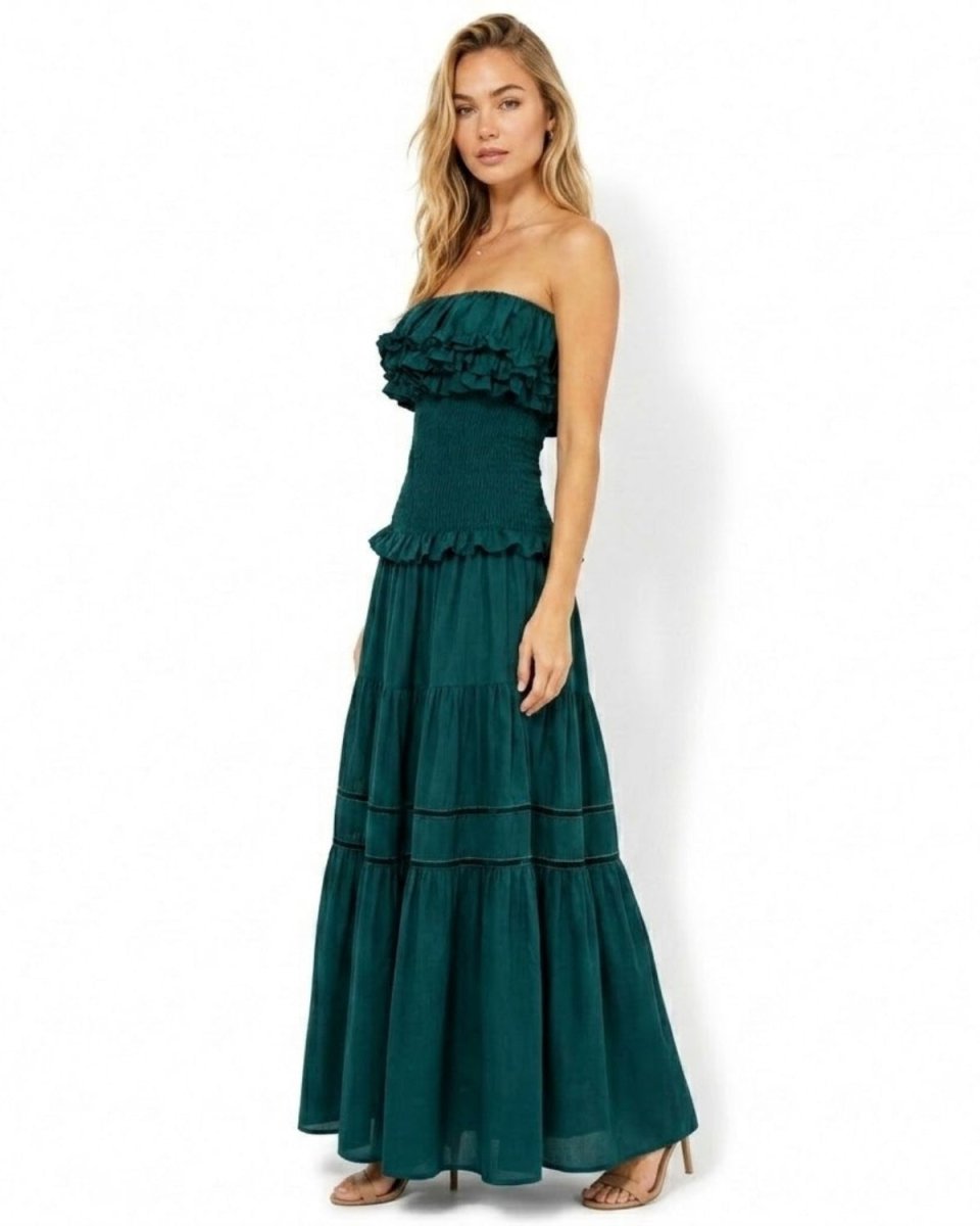 Side profile of woman in luxury dark green bandeau maxi dress showing flowing tiered skirt and form-fitting smocked waist.