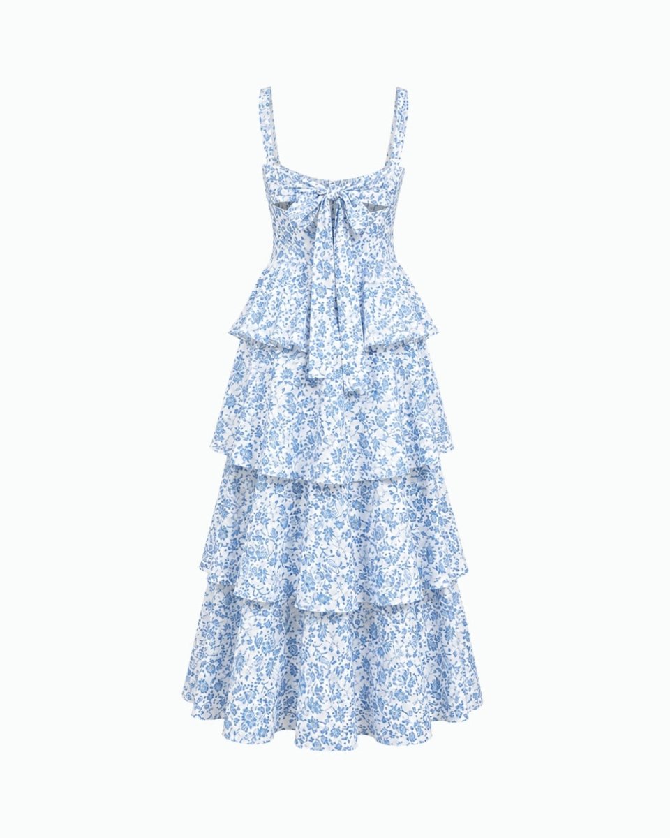 A light blue and white floral print tiered maxi dress with thin shoulder straps, a sweetheart neckline, and a bow detail at the center bust, shown against a plain white background.