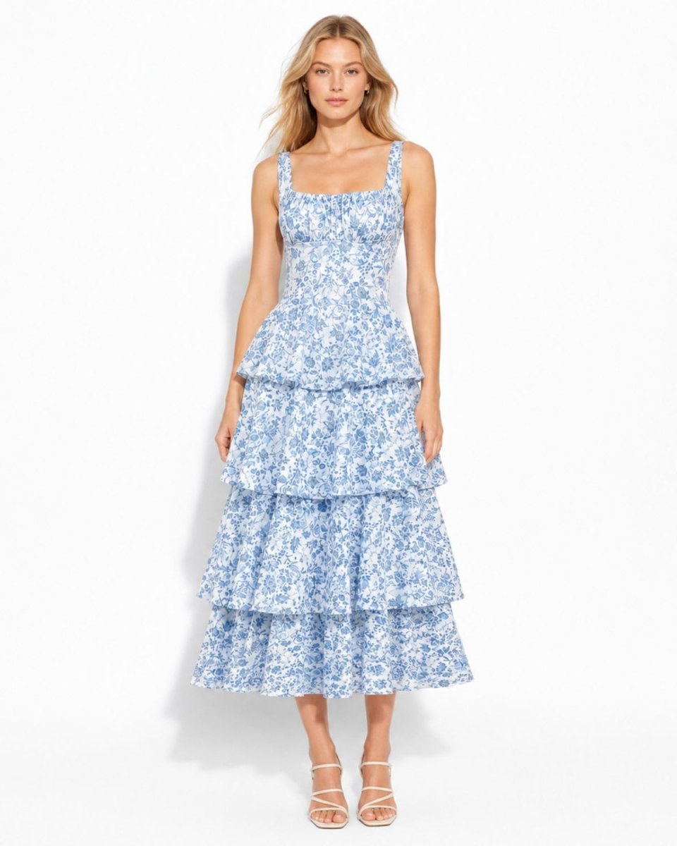 A woman modeling a sleeveless, tiered midi dress with a blue and white floral pattern against a plain white studio background.