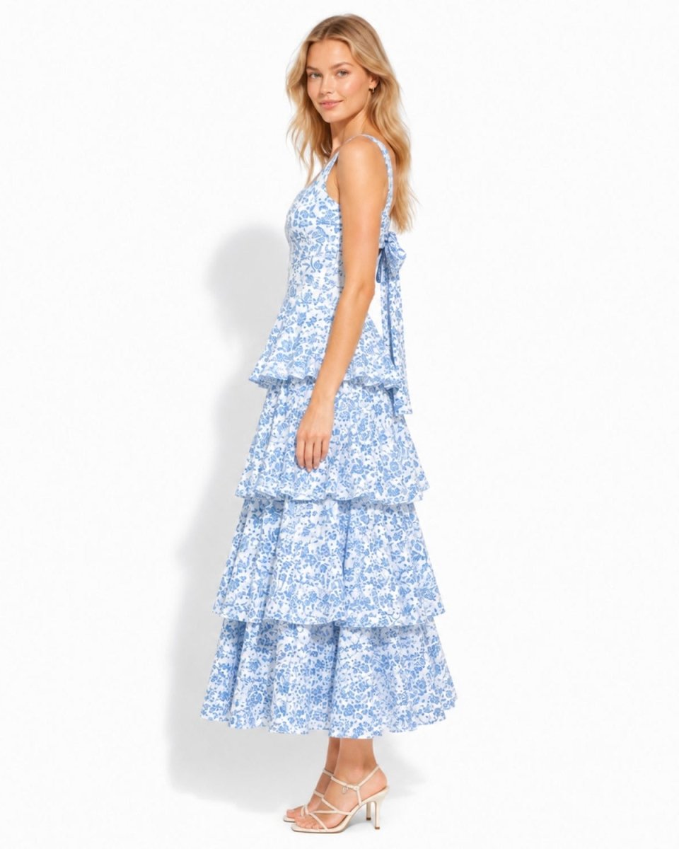 A woman modeling a sleeveless, tiered maxi dress with a light blue and white floral pattern, photographed against a clean white studio background.