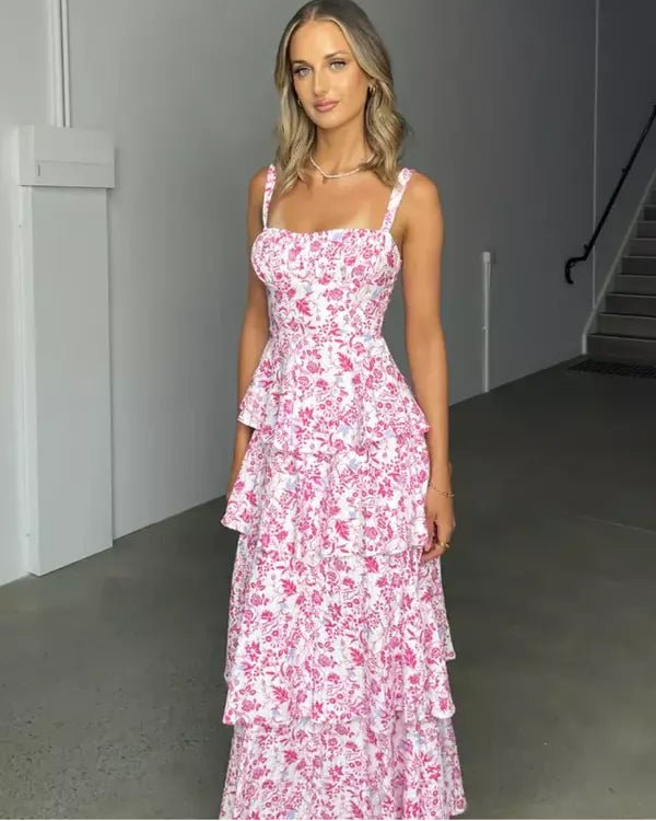 Model wearing the Denise pink floral tiered midi dress with a square neckline and open-back bow detail at a garden party