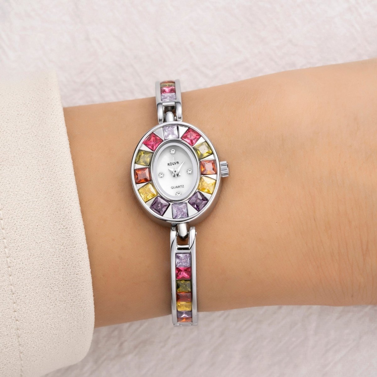 Top down lifestyle view of the colorful Kouvr gemstone style oval watch being modeled beautifully on a woman's wrist against a textured background