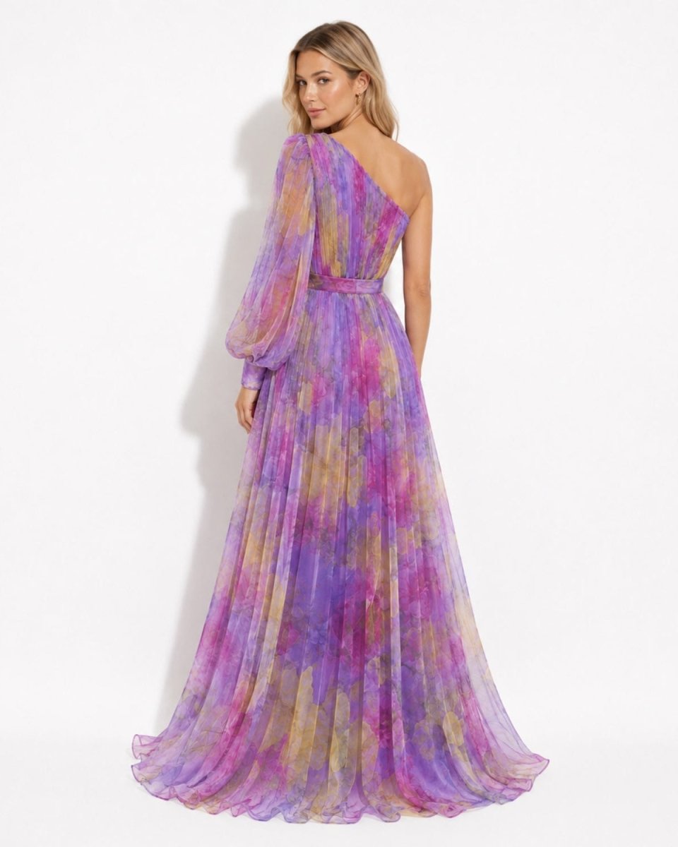 A woman modeling a floor-length one-shoulder chiffon gown with a purple, pink, and yellow tie-dye pattern, shown from the back against a white studio background.