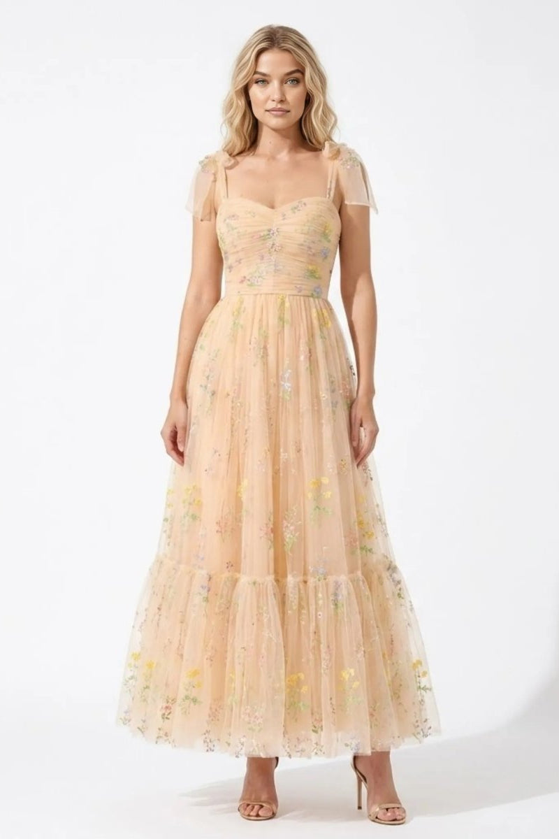 Woman wearing Fenlo Form floral embroidered tulle maxi dress in champagne featuring tie shoulder straps and sweetheart neckline.