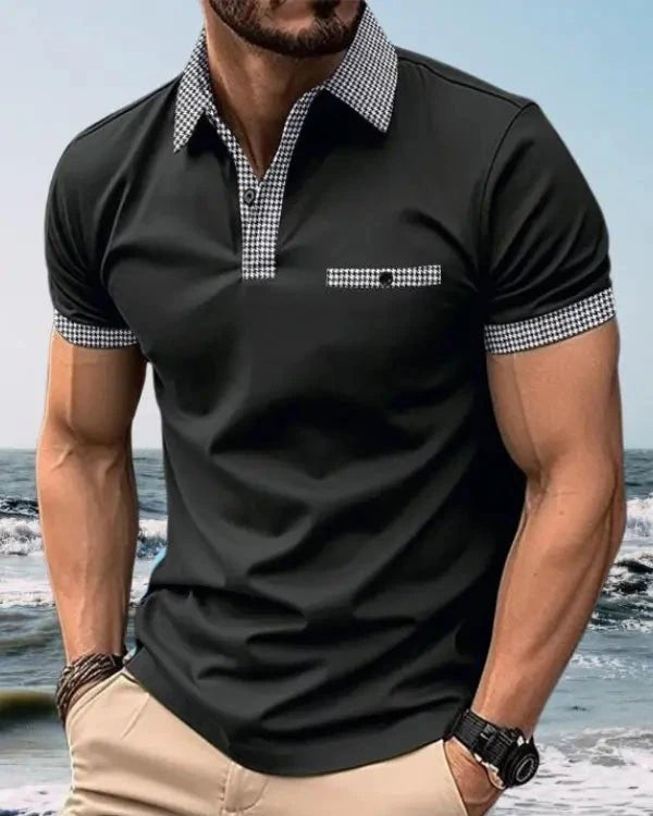 Man wearing a black polo shirt with checkered collar and cuffs on a beach.