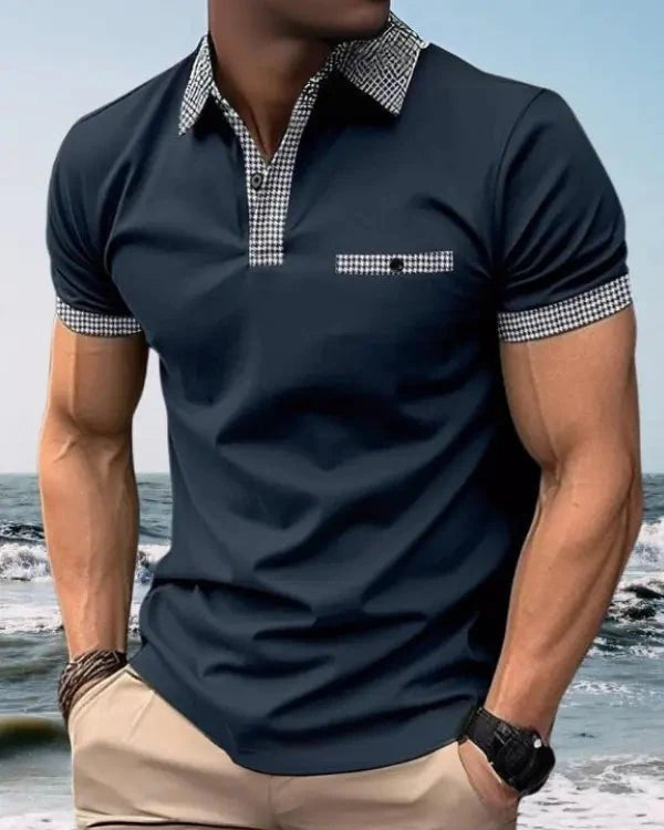 Man wearing a navy polo shirt with checkered collar and cuffs on a beach.