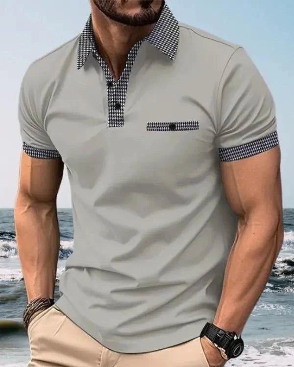 Man wearing a light gray polo shirt with checkered collar and cuffs, standing on a beach.