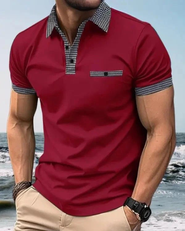 Man wearing a red polo shirt with checkered collar and cuffs, standing on a beach.