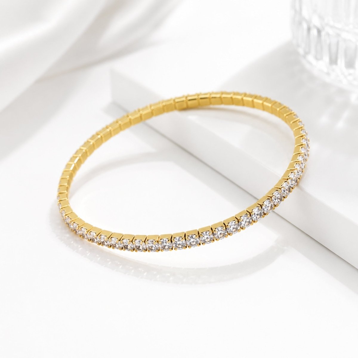 Angled view of a continuous gold plated elastic tennis bracelet featuring 3mm cubic zirconia stones resting on a white marble display block.
