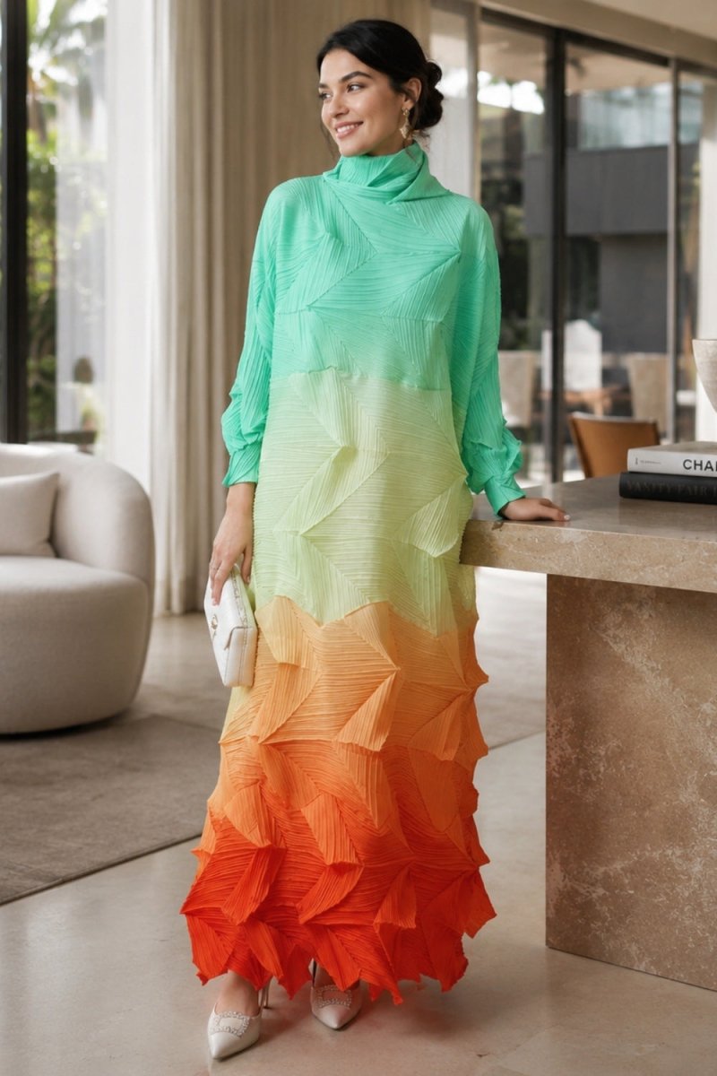 A woman models a long-sleeve turtleneck maxi dress with a vibrant vertical ombre gradient transitioning from mint green to pale yellow, orange, and bright red, styled in a modern indoor setting.