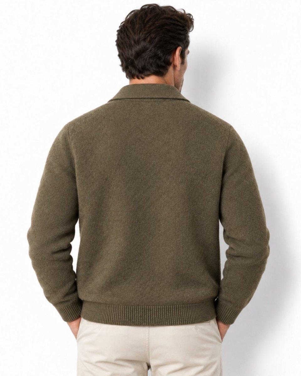 A man viewed from behind wearing an olive green knit sweater and light beige trousers, standing against a plain white studio background.