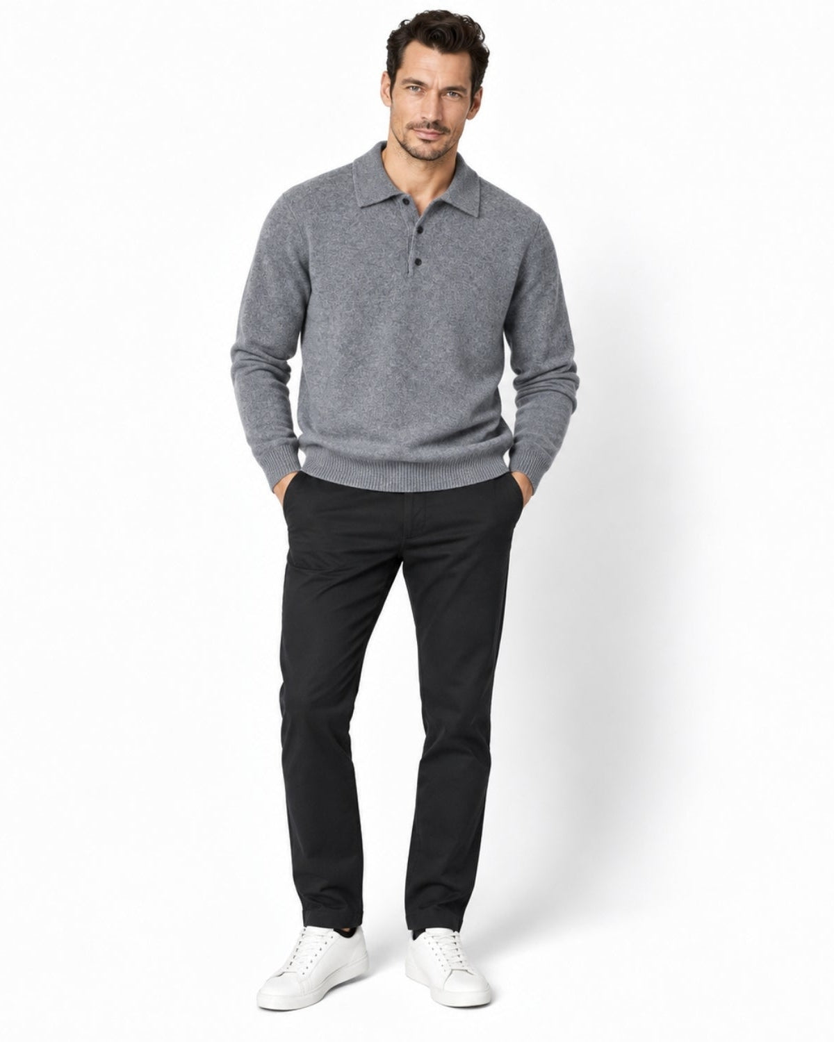 A man modeling a gray long-sleeve polo knit sweater, paired with black trousers and white sneakers, standing against a clean white studio background.