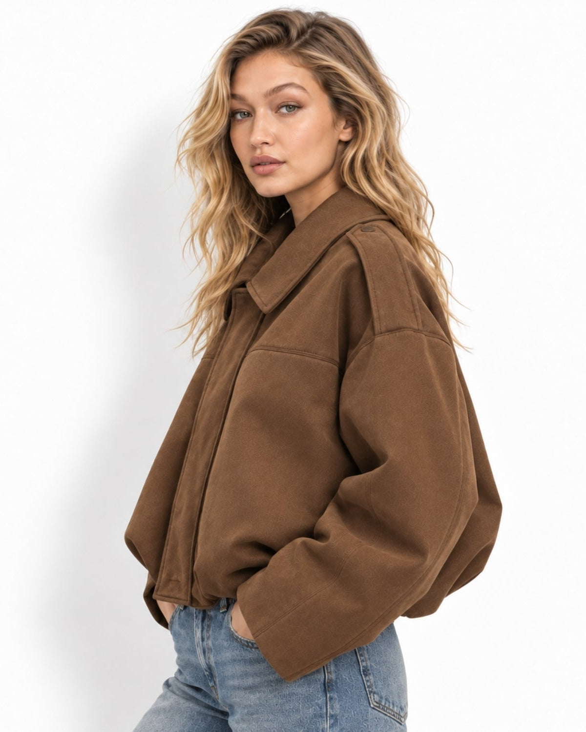 A woman wearing an oversized brown jacket and light blue jeans, photographed against a clean white studio background.