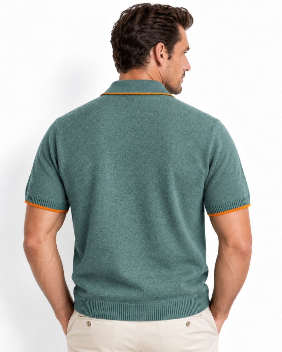A man viewed from the back wearing a short-sleeve knit polo shirt in muted teal green with thin orange trim at the collar and sleeve cuffs, paired with light beige pants against a clean white studio background.