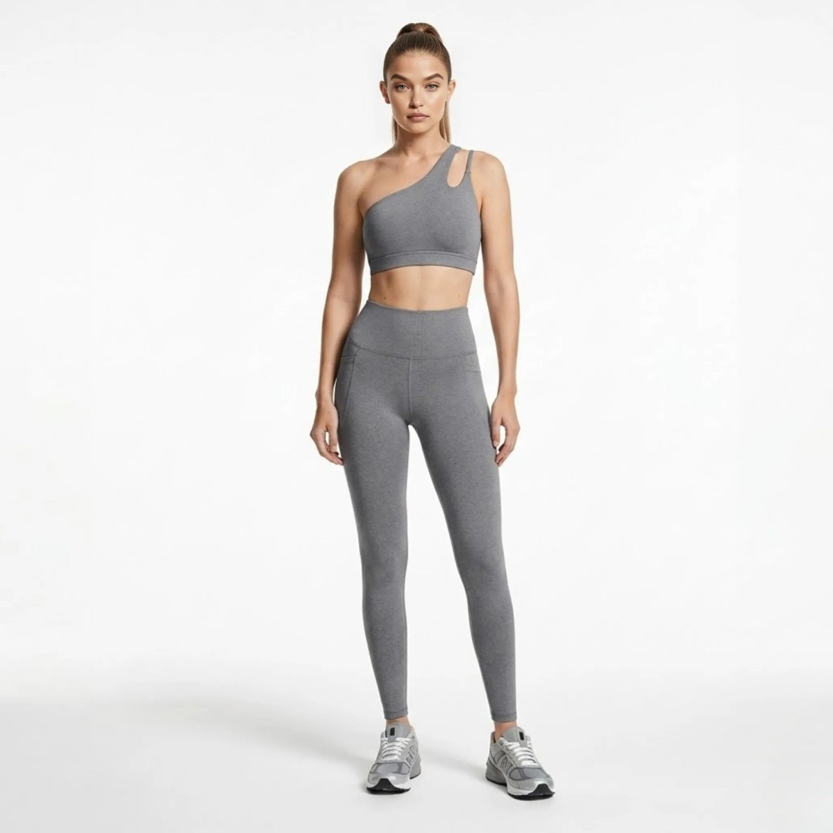 Woman wearing Kouvr grey asymmetrical one shoulder sports bra and high waisted pocket leggings activewear set looking forward.