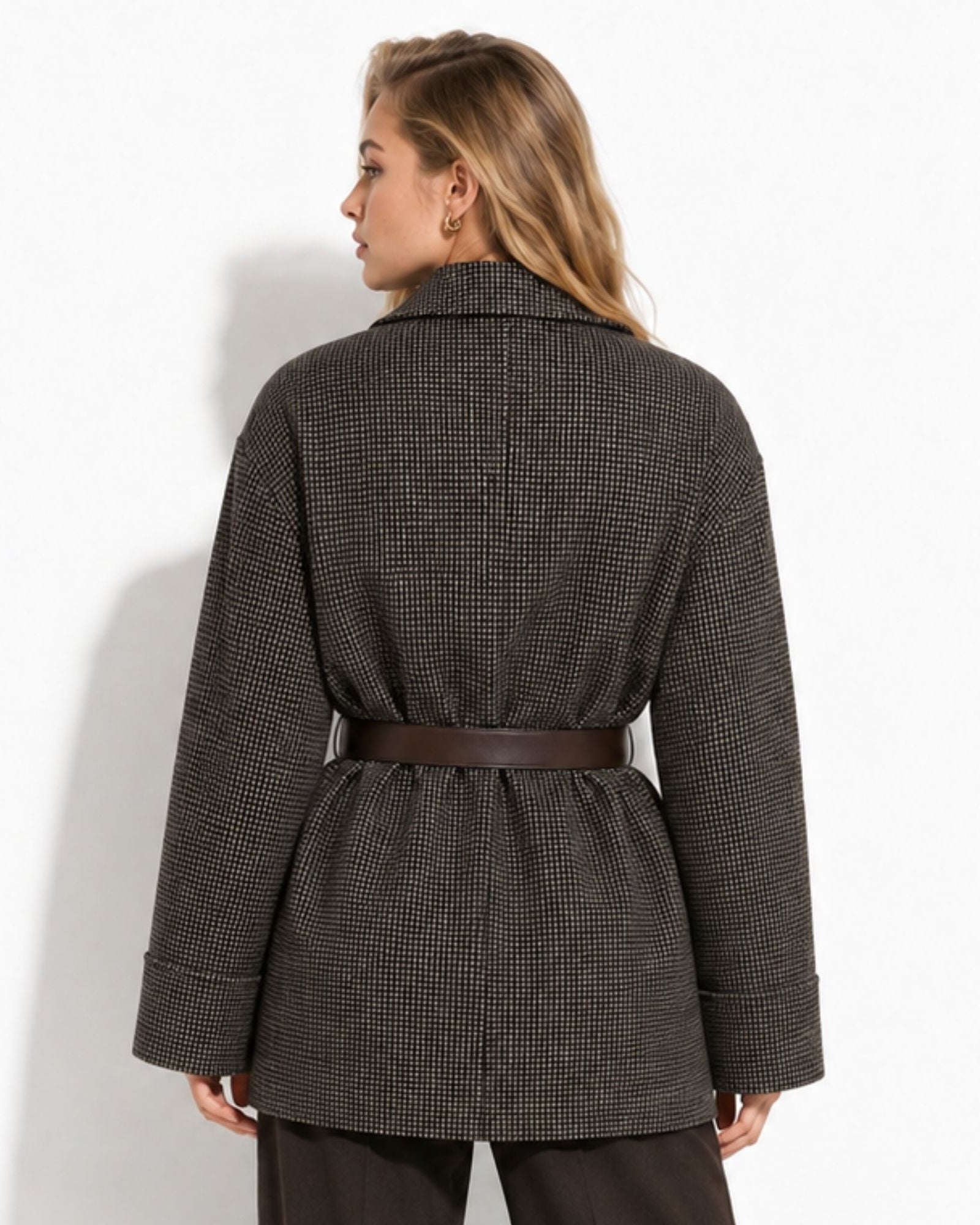 A woman shown from the back wearing a dark brown and black houndstooth patterned coat with a brown belt, set against a plain white studio background.