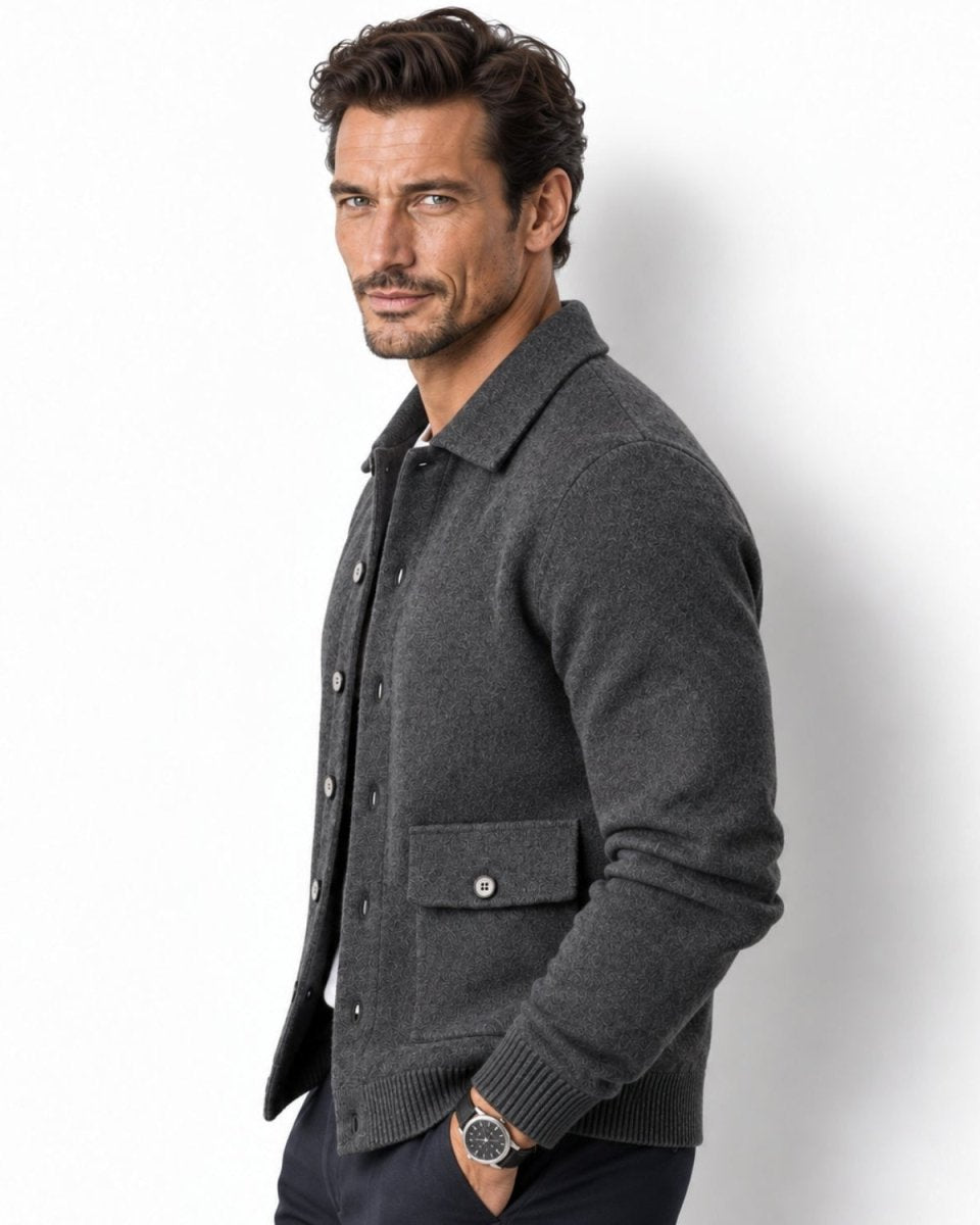 A man wearing a dark gray knit button-front cardigan with a collar and flap pocket, posed against a clean white studio background.