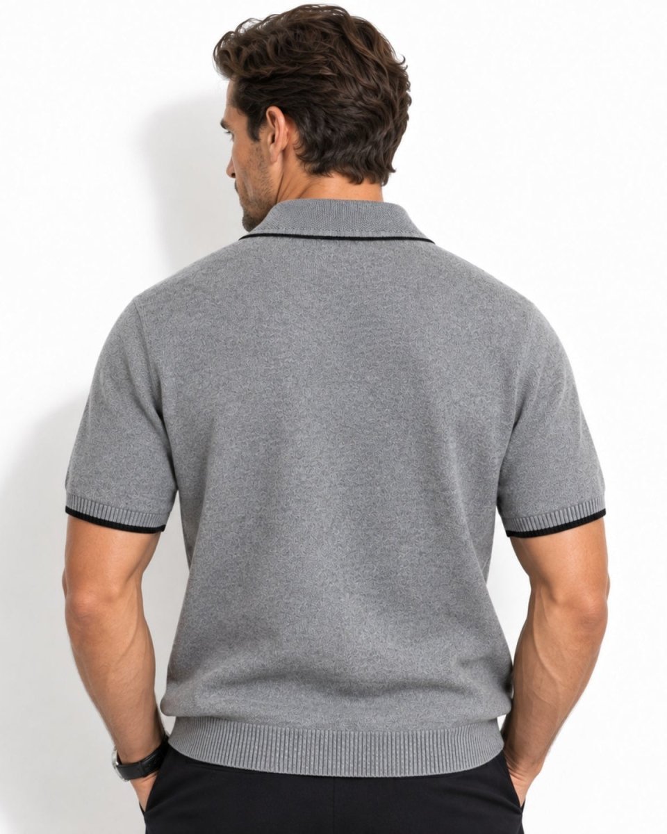 A man viewed from the back wearing a gray short-sleeve knit polo shirt with black trim on the collar and sleeve cuffs, paired with black pants, against a plain white studio background.