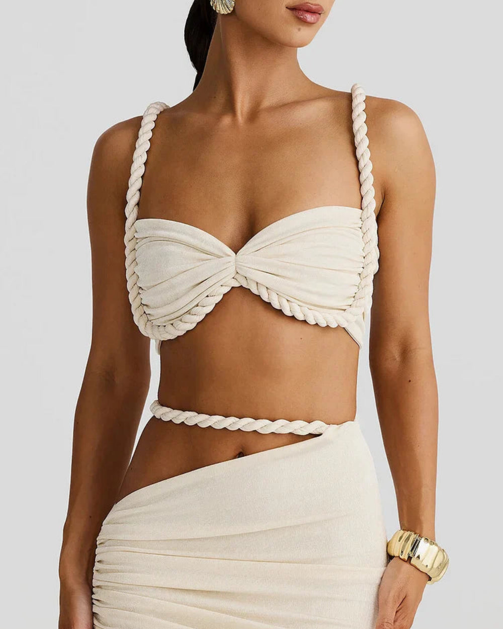 Model wearing The Thelma Set, a beige two-piece Grecian outfit featuring a rope detail bralette top and a ruched asymmetrical maxi skirt