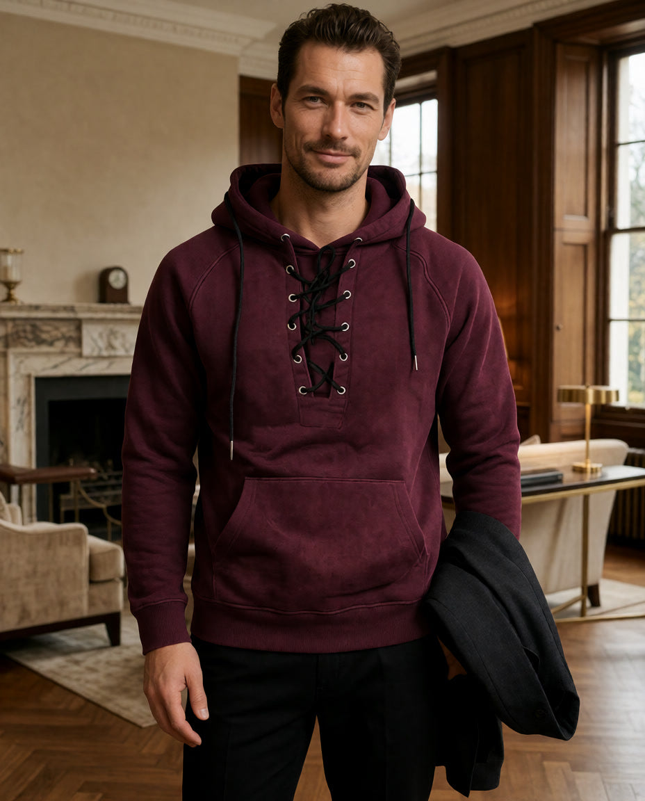 Ein Model trägt den burgunderroten Cannon Kapuzenpullover in einem Raum mit Kamin und hält eine schwarze Jacke.