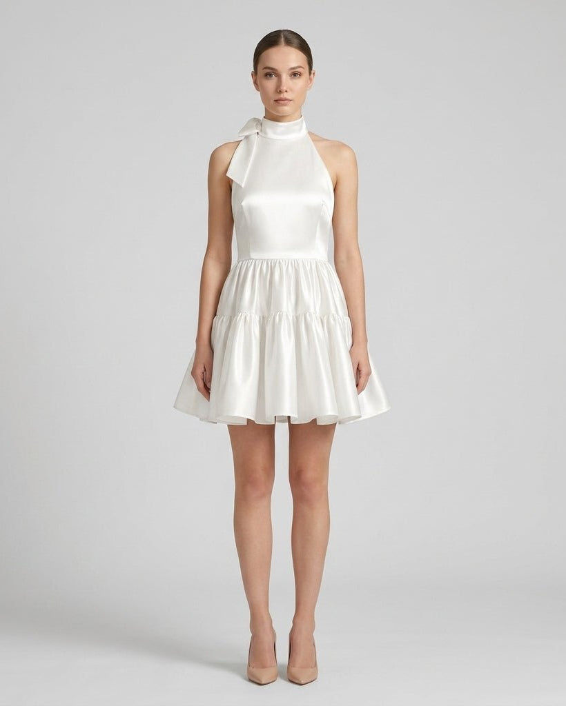 Front view of a female model wearing a white satin halter neck mini dress with a tiered ruffle skirt.