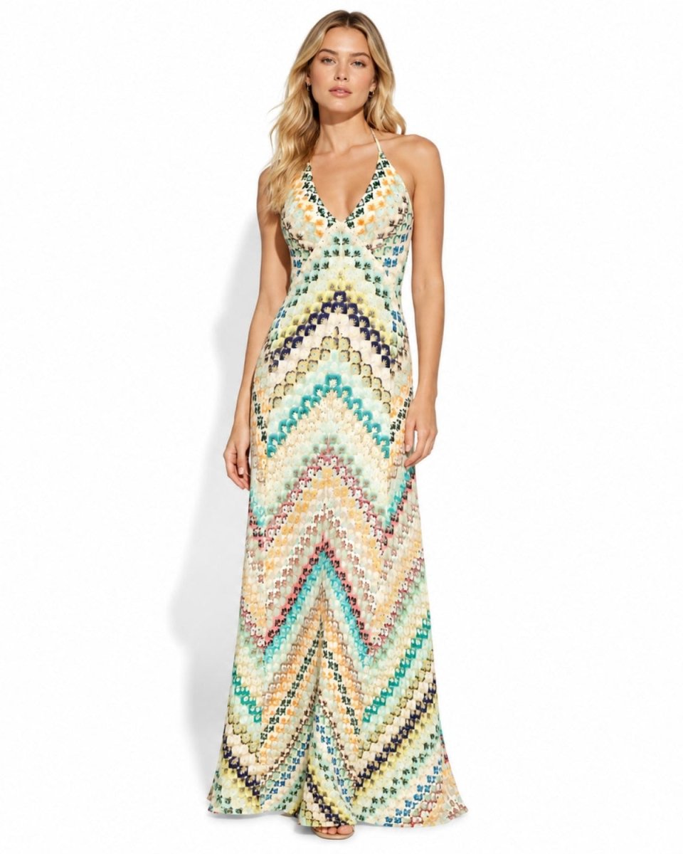 A woman modeling a sleeveless, floor-length maxi dress with a colorful chevron pattern in shades of teal, yellow, blue, pink, and beige against a plain white studio background.