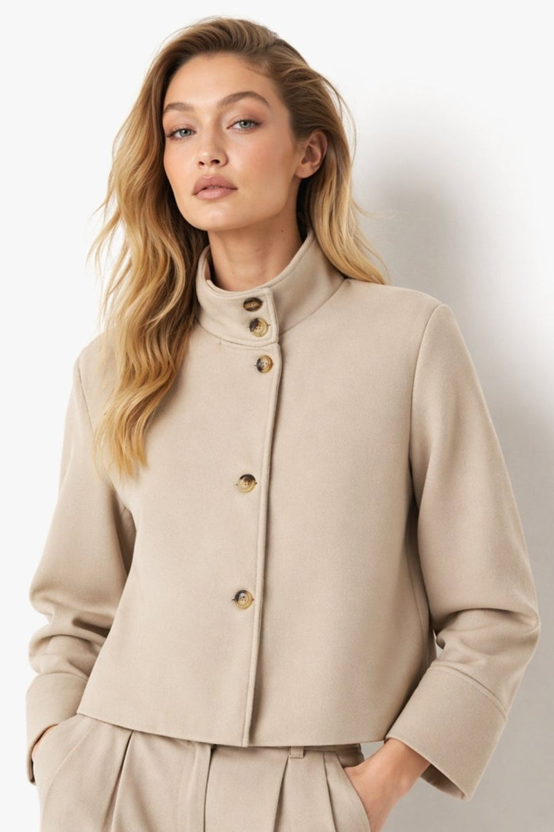 Woman wearing a khaki wool blend cropped stand collar jacket with tortoiseshell buttons by Fenlo Form.