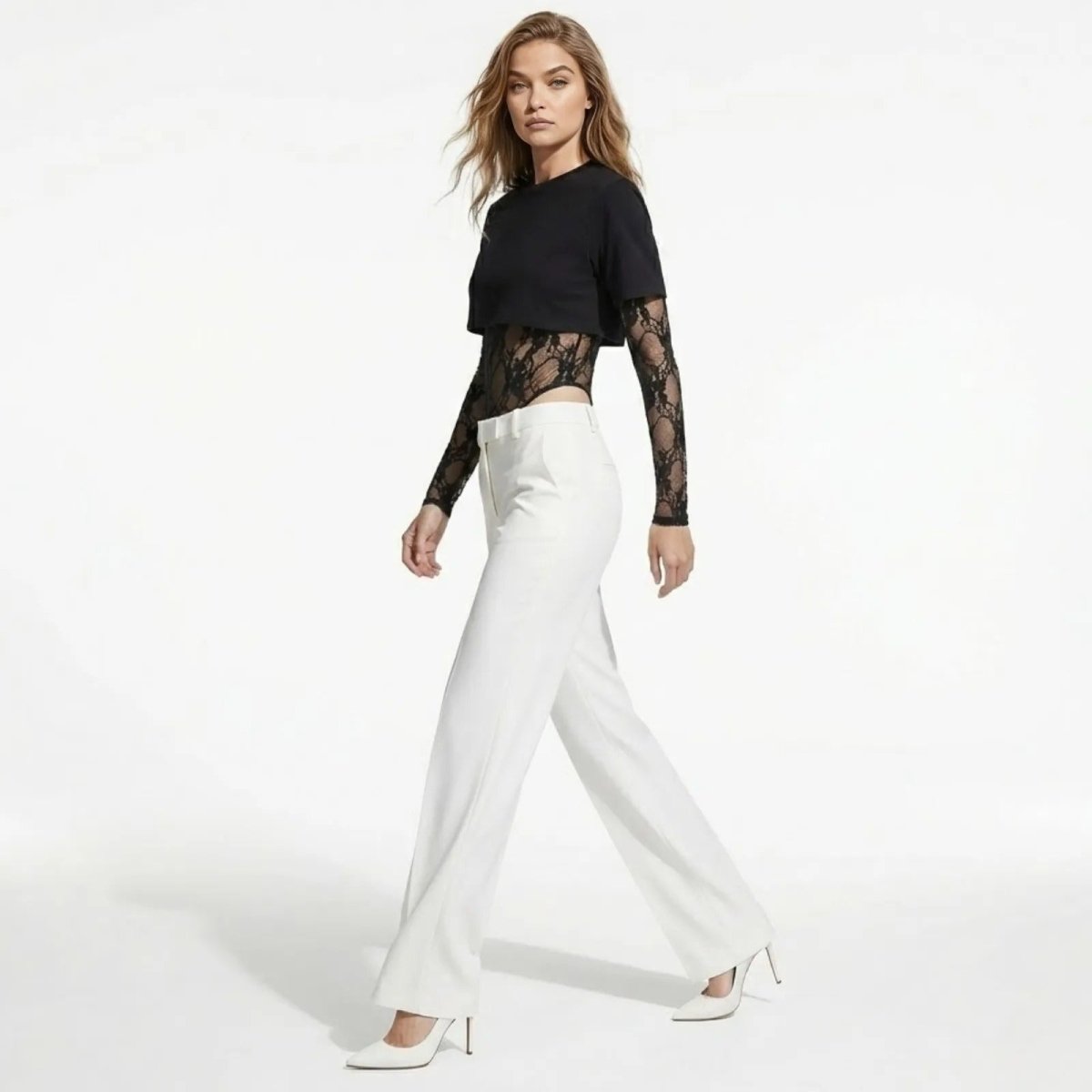 Model in a walking motion showing the side profile of the Kouvr Fashion Angelique black lace long sleeve bodysuit and white wide-leg pants.