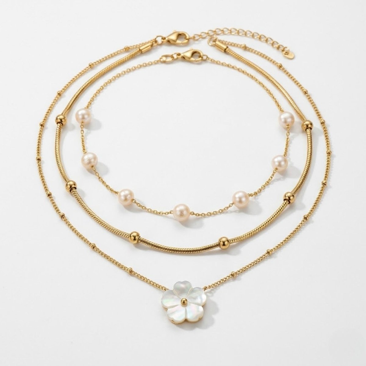 Kouvr Brisa  three-piece gold layered necklace set featuring a pearl strand, a gold bead snake chain, and a mother-of-pearl flower pendant on a white background.