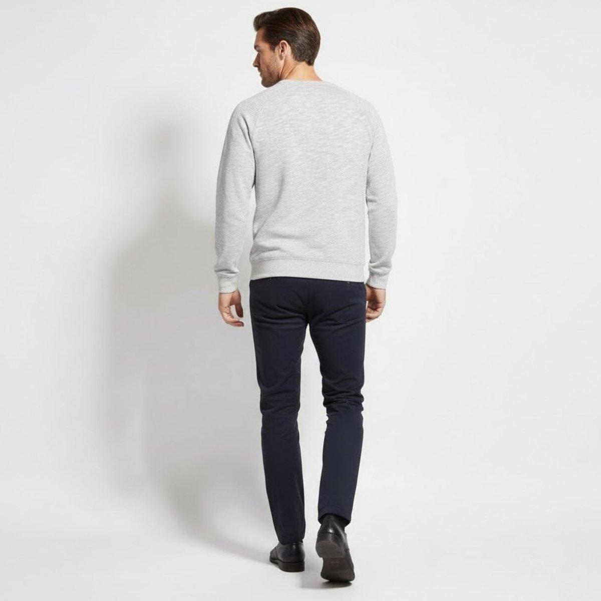 Back view of a male model wearing the Kouvr Deacon Crewneck Sweatshirt in heather light grey, highlighting the raglan sleeve construction.
 
