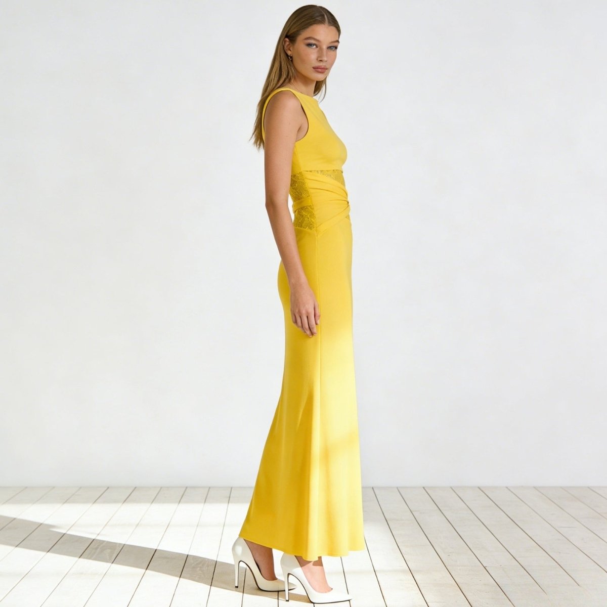 Side profile of a woman in a pale yellow bodycon midi dress showing the asymmetrical lace cut out detail at the waist.