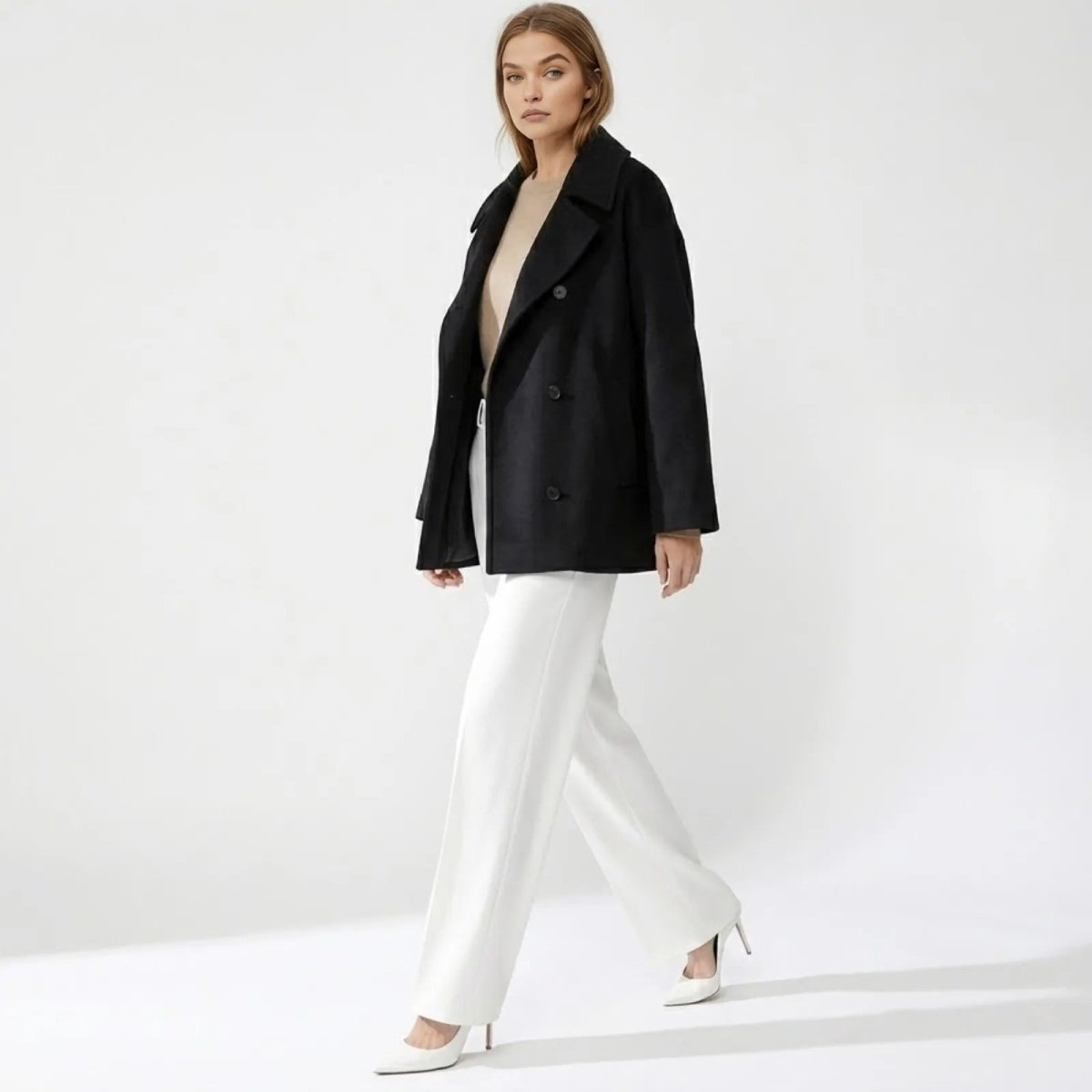 Side profile of a model walking in the Kouvr Fashion oversized black wool peacoat, showing its fluid movement and silhouette.
