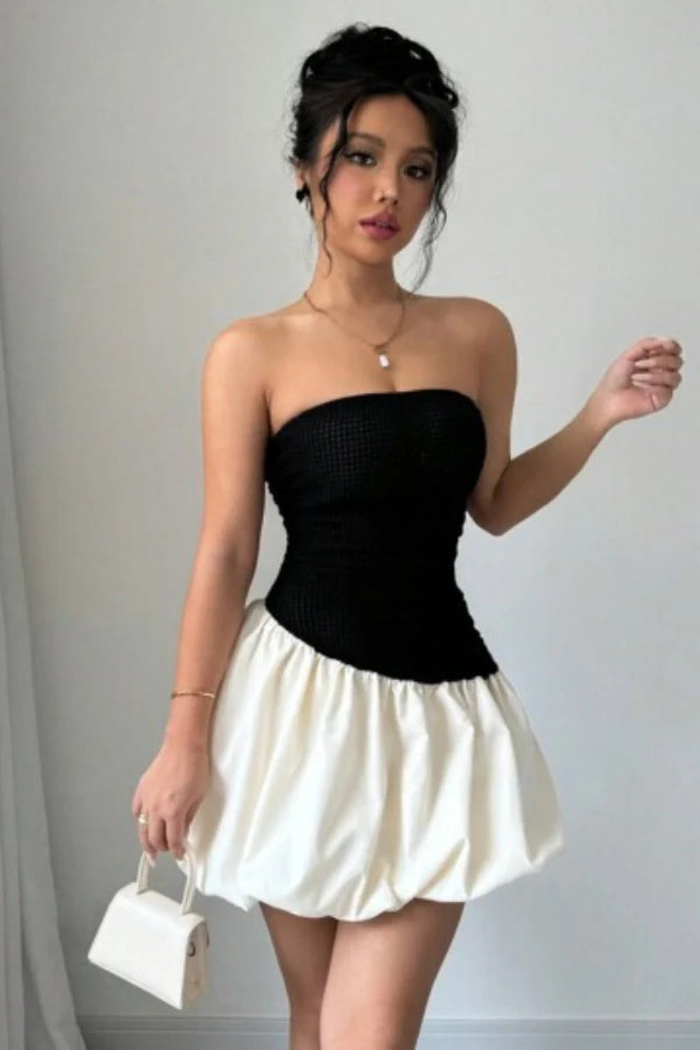 Model wearing Kouvr Fashion strapless black and white bubble hem mini dress against background