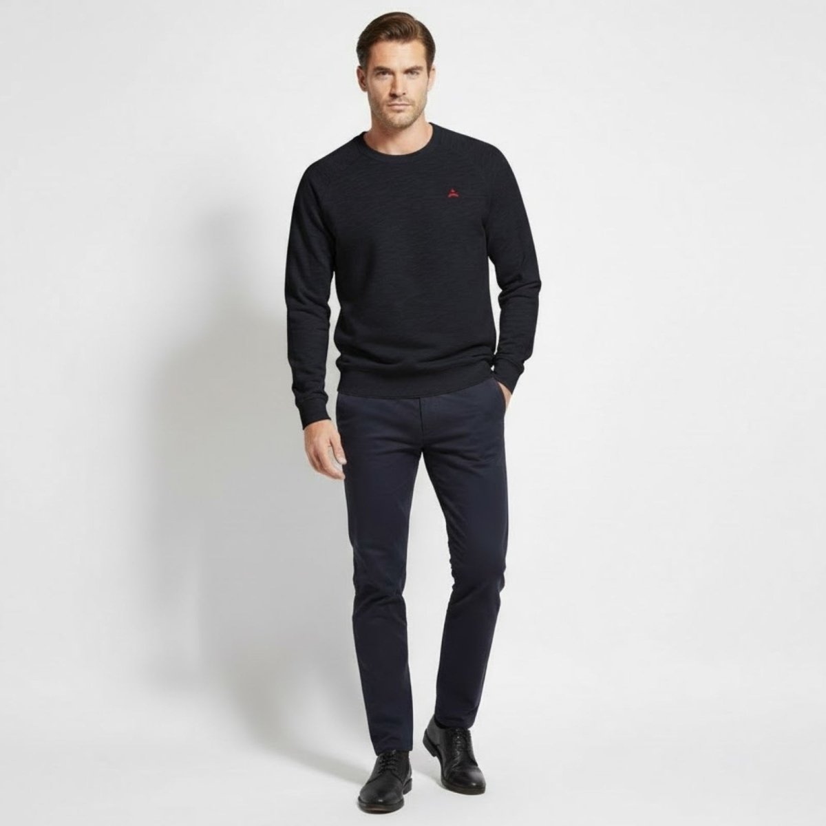 Male model wearing the Kouvr Fashion Deaconnavy blue raglan sleeve sweater with dark trousers, facing forward in a studio.
