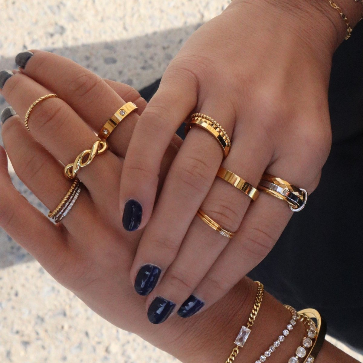 Woman with dark nails wearing multiple gold Kouvr rings including the trio stacking set.