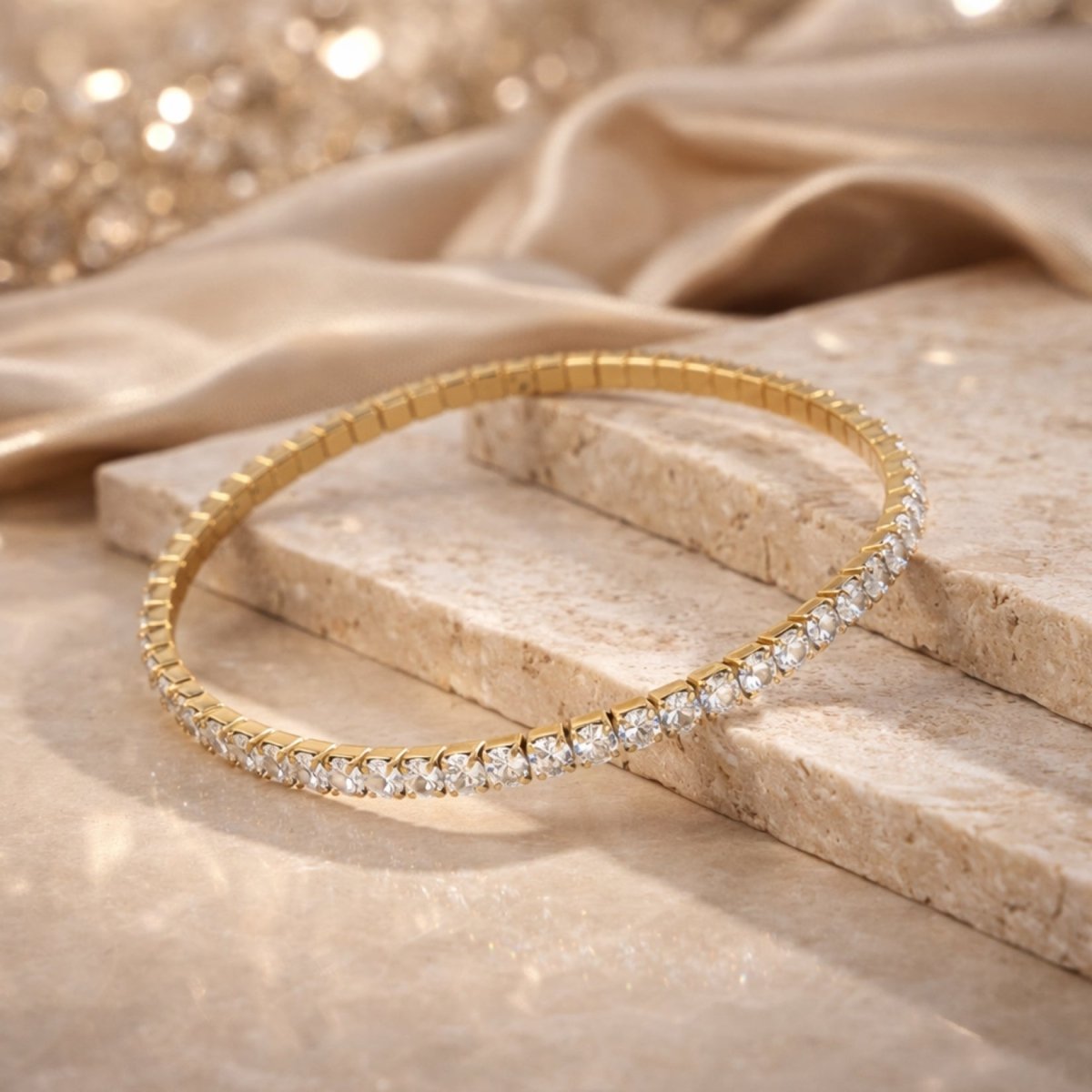  Lifestyle product shot of the Kouvr gold stretch tennis bracelet resting on beige travertine stone with a silk background.