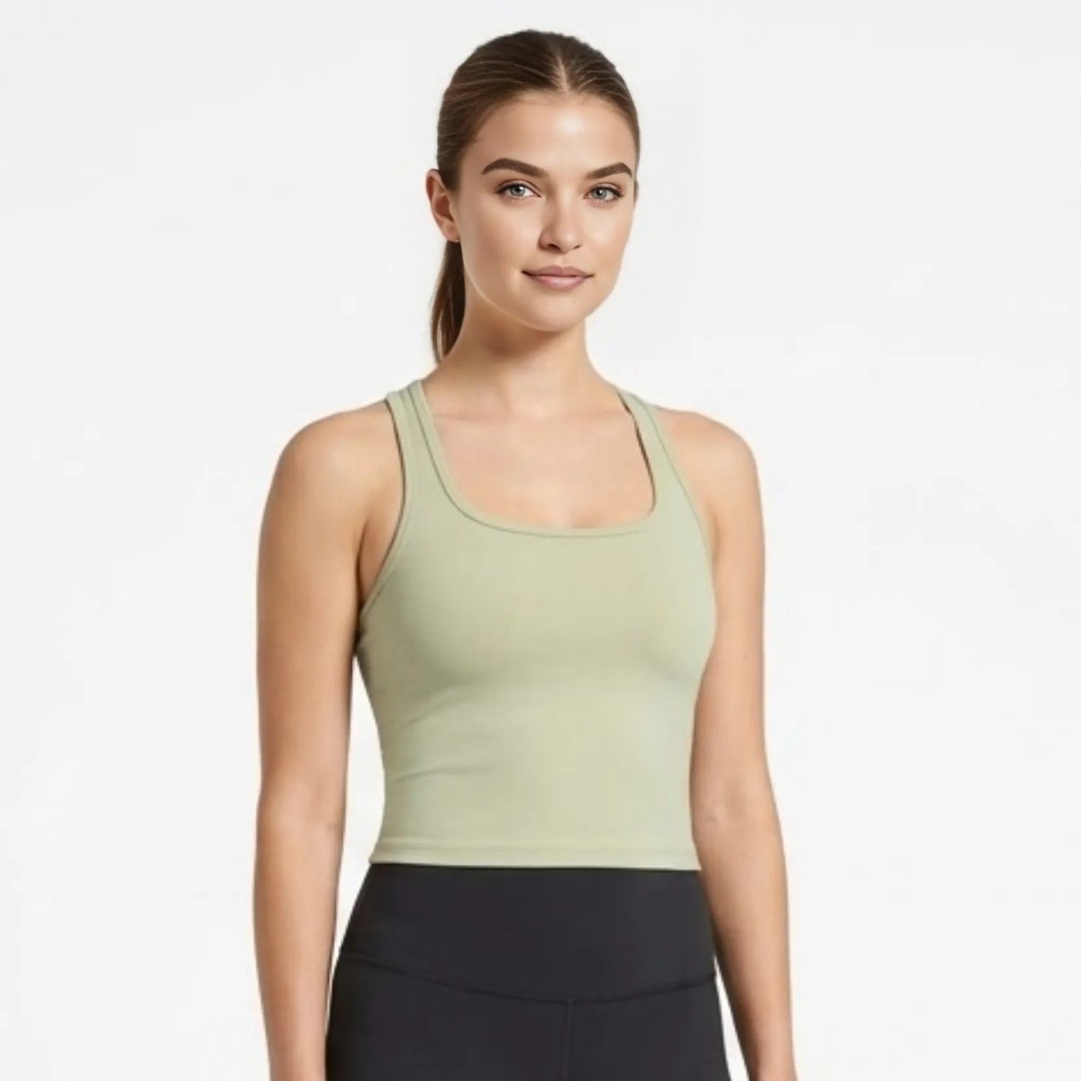 Woman wearing Kouvr luxury green sculpting racerback crop top in front view, styled with black athletic leggings.