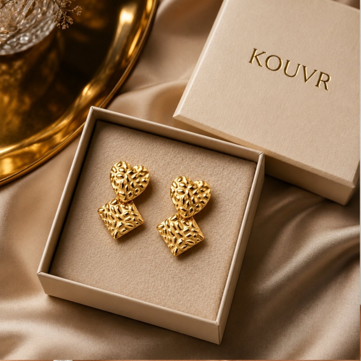 Kouvr hammered gold heart and diamond drop statement earrings resting elegantly in a luxury beige presentation box