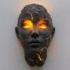 Front-on view of the illuminated wall art lamp by Kouvr, highlighting the symmetrical glowing eyes and the artistic network of cracks across the face.