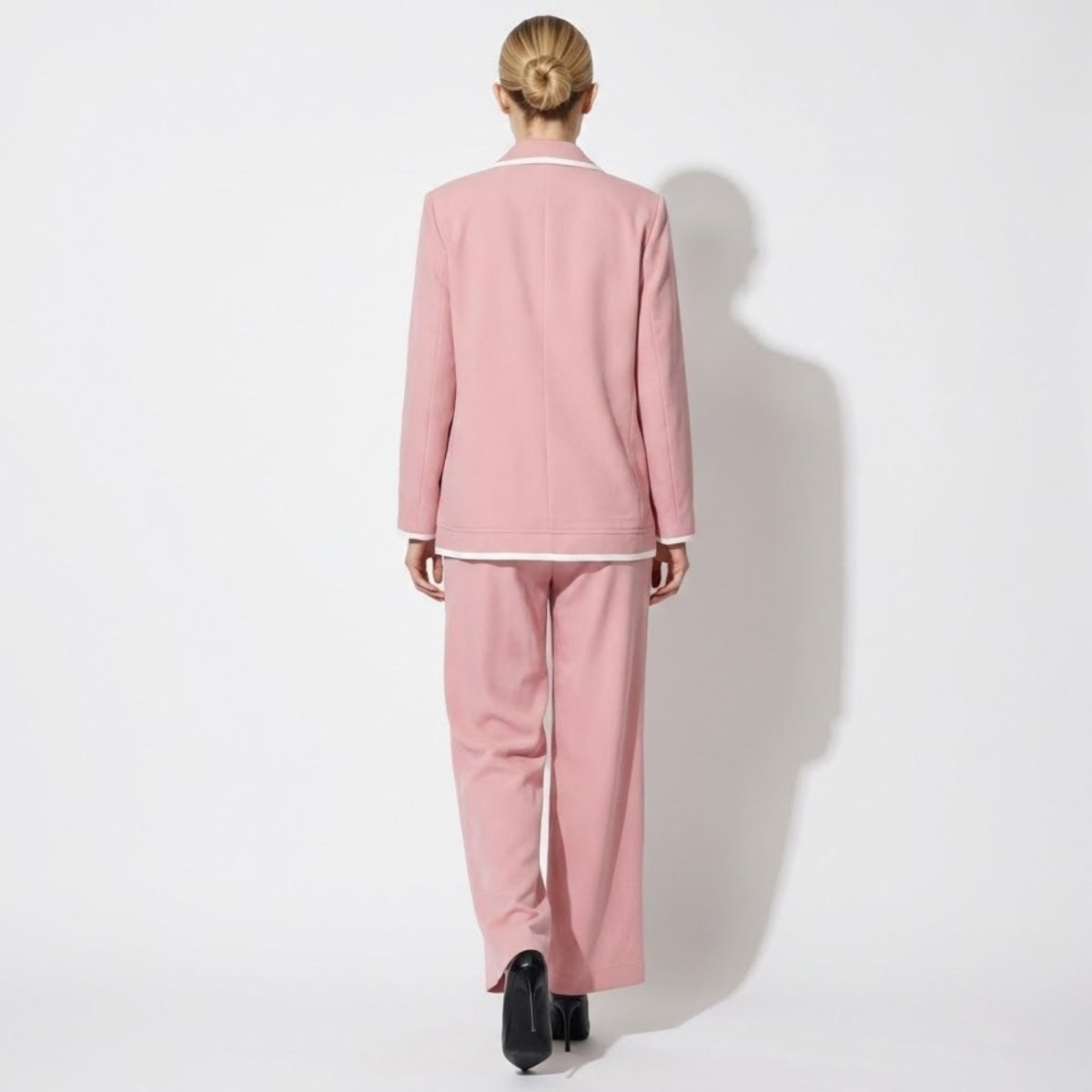 Back view of the Kouvr Lucia Set pink blazer and trouser suit, highlighting the clean lines, expert tailoring, and contrast white piping detail on the collar.
