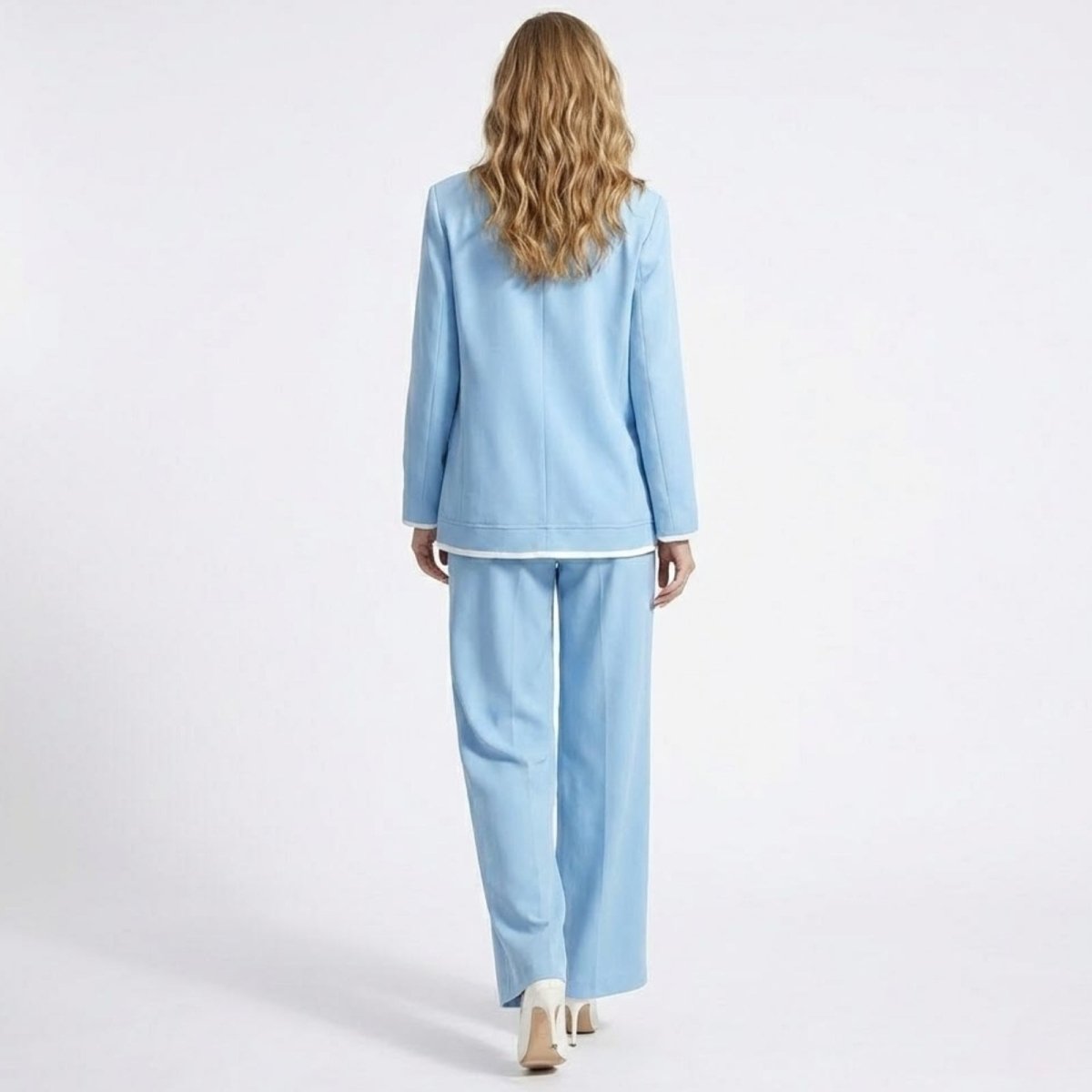 Back view of a model in the Kouvr Lucia Set sky blue pant suit, highlighting the clean lines and white piping detail on the blazer hem.
