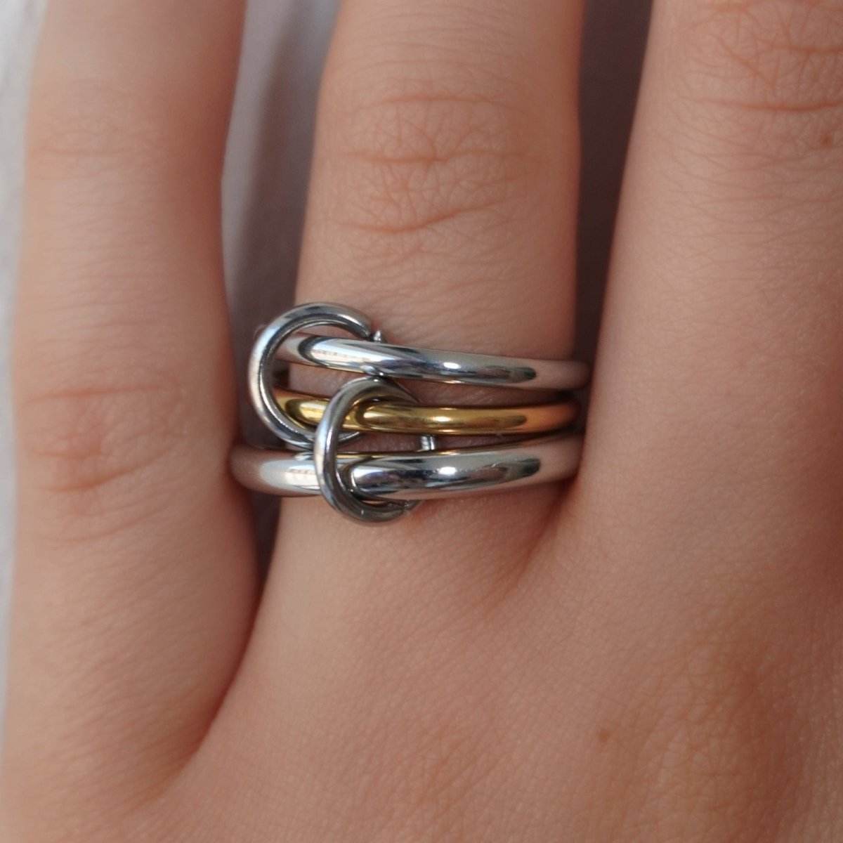 A close-up of the Kouvr Mavis interlocking statement ring in polished sterling silver with a gold accent band on a finger.