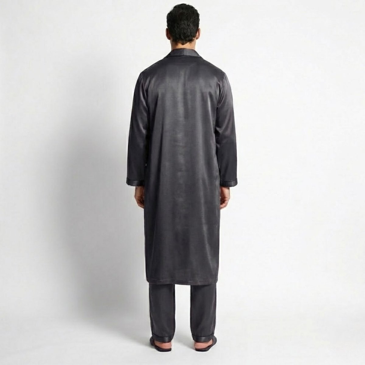 Back view of a male model wearing the full-length Kouvr dark grey satin robe over the matching pajama set, displaying the garment's length and fit.
