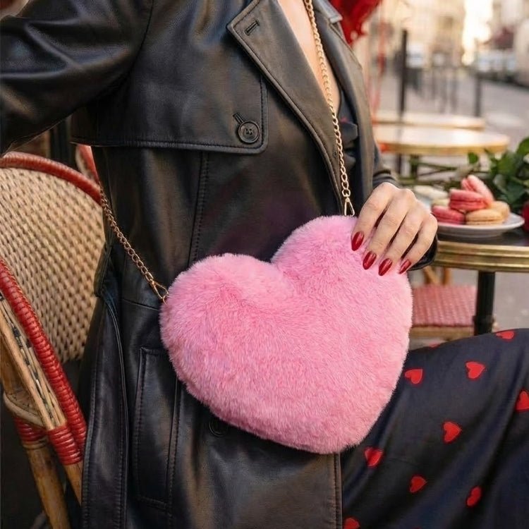 Woman in a black leather trench coat sitting at a Parisian cafe, holding a plush pink heart-shaped bag with a gold chain.