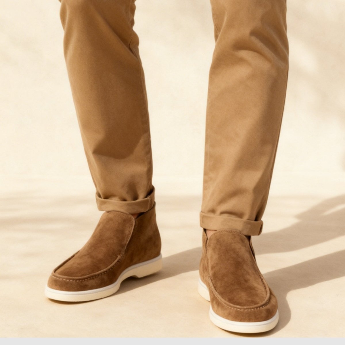 Kouvr suede ankle loafer boots with tan chino pants.
Side view of black Italian suede slip-on boots with a contrasting white sole, worn by a model. 