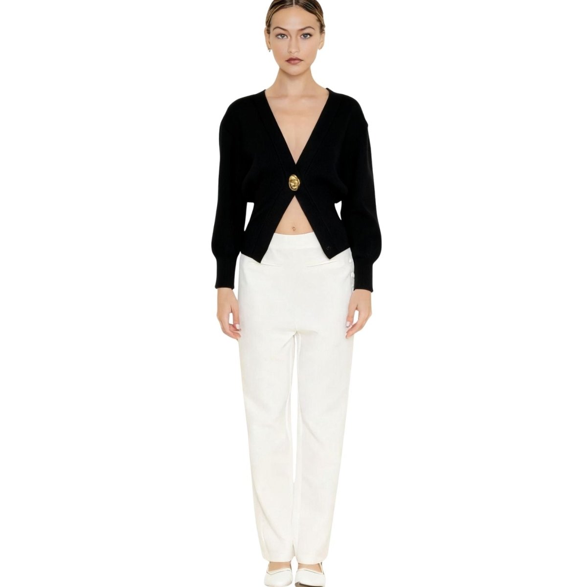 Model wearing the Kouvr black sculptural knit v-neck cardigan with a single gold button, paired with white trousers.