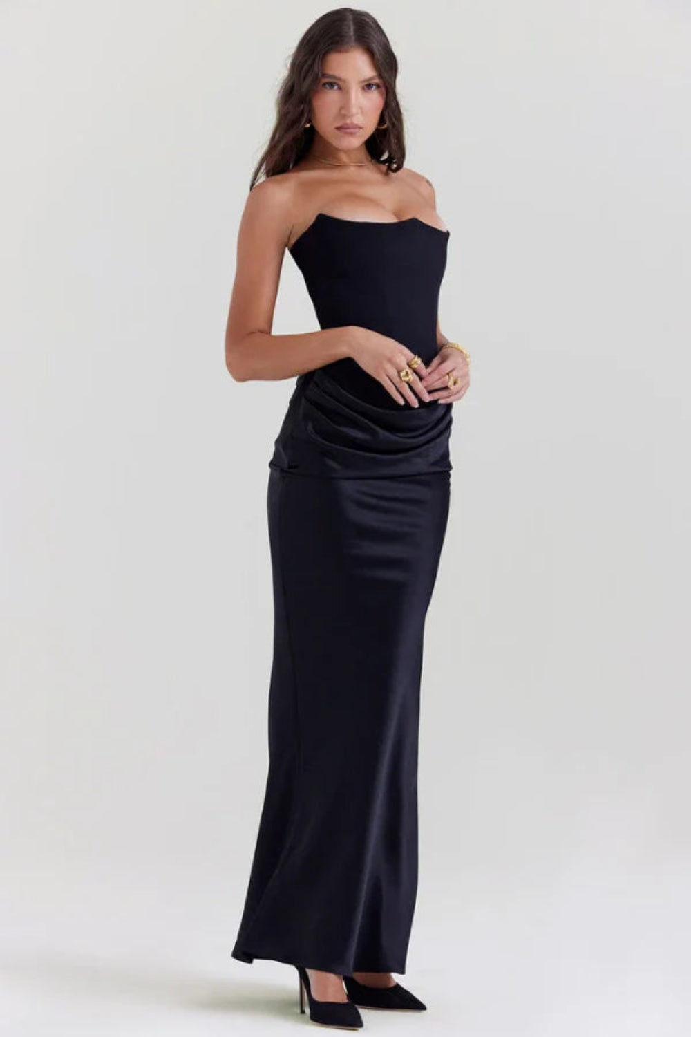 Side angle view of a model in the Sloane black satin evening gown, showcasing the fitted silhouette and gold accessories.
