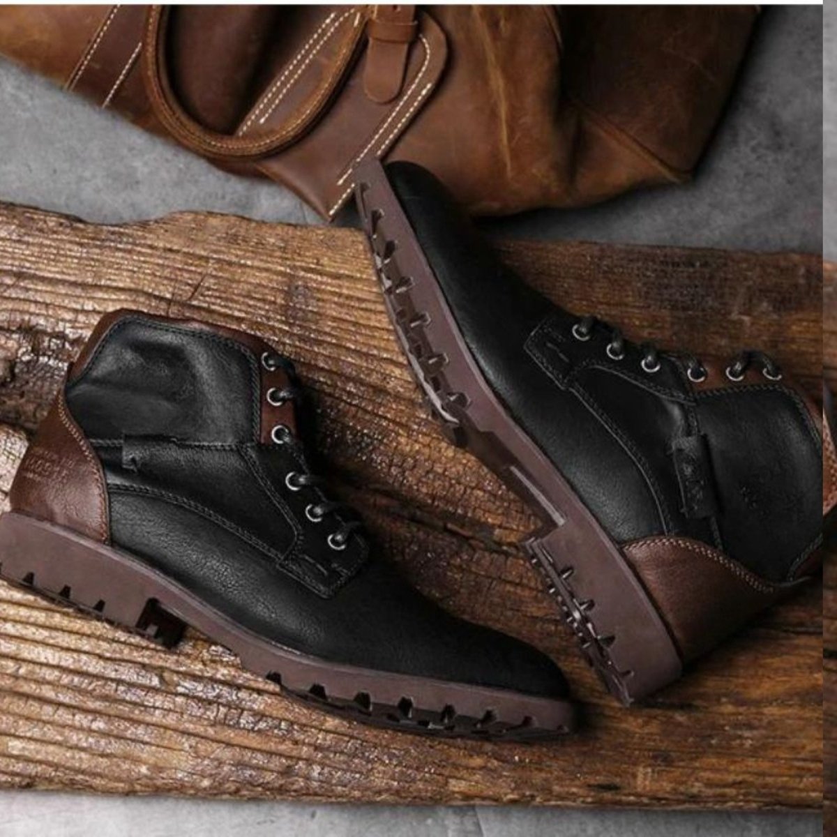 Pair of brown and black leather boots on a wooden surface with a brown jacket in the background.