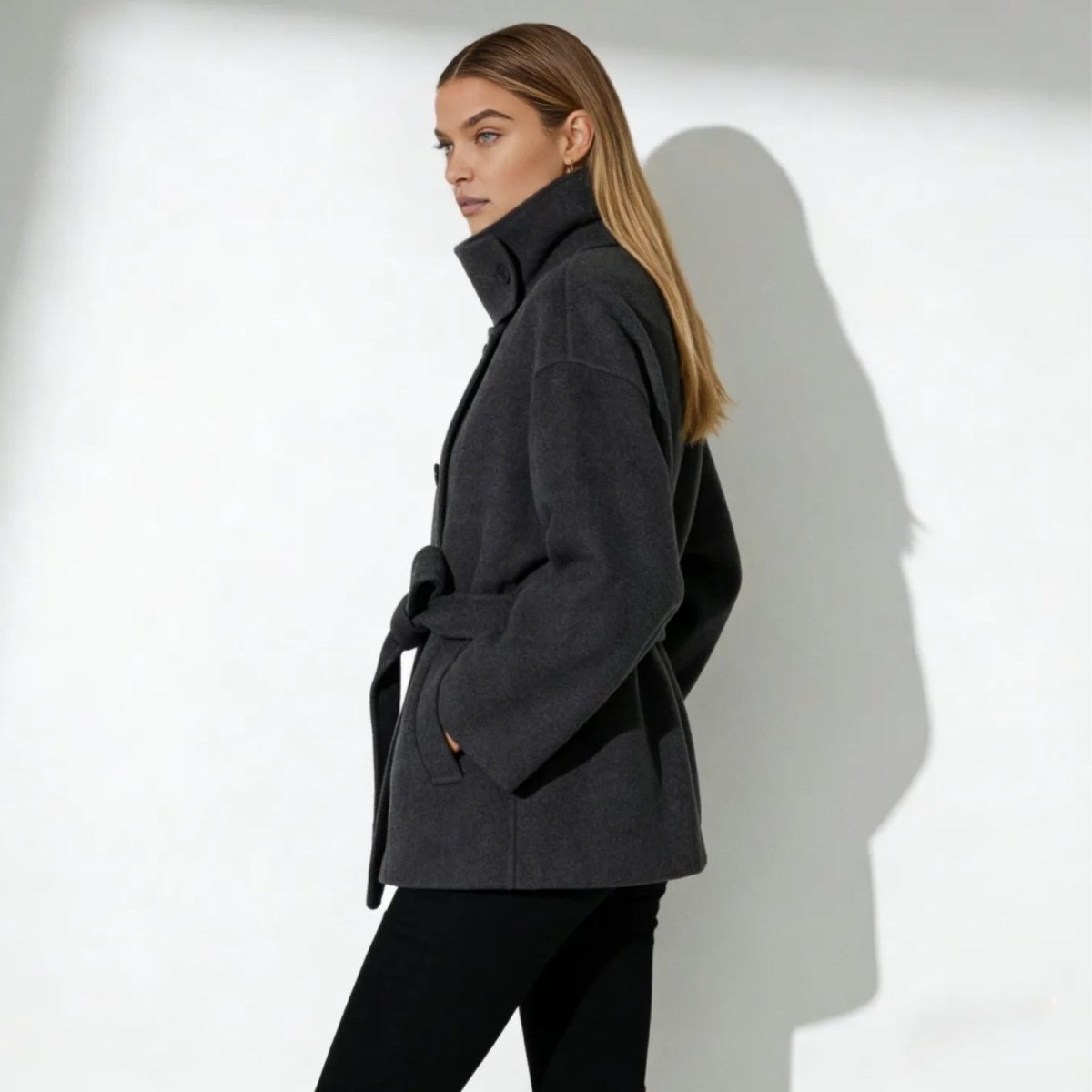 Side profile of the Kouvr Verna short wool coat showing its silhouette and high collar detail.
